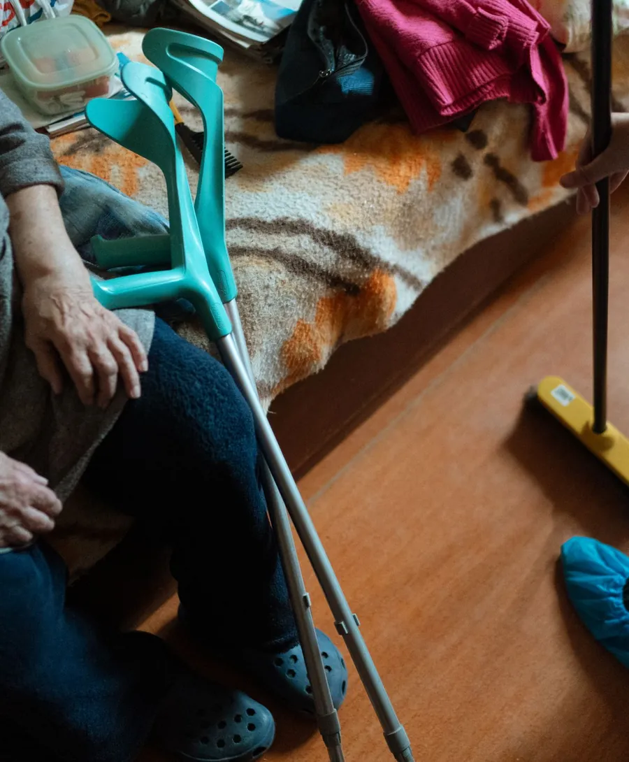 Hulp in huis: er wordt geveegd terwijl een oudere vrouw met kruk op de bank zit