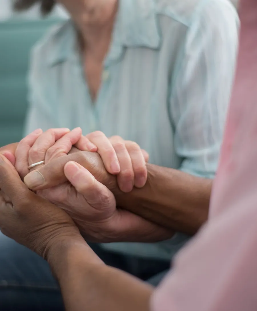 Handen van een zorgverlener rusten geruststellend op de handen van een oudere vrouw
