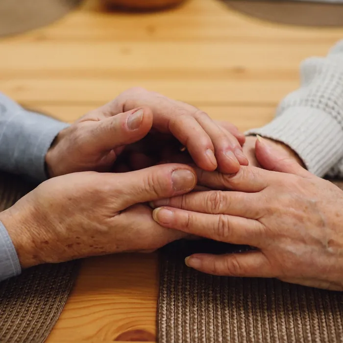 Twee paar handen die elkaar vasthouden op een houten tafel