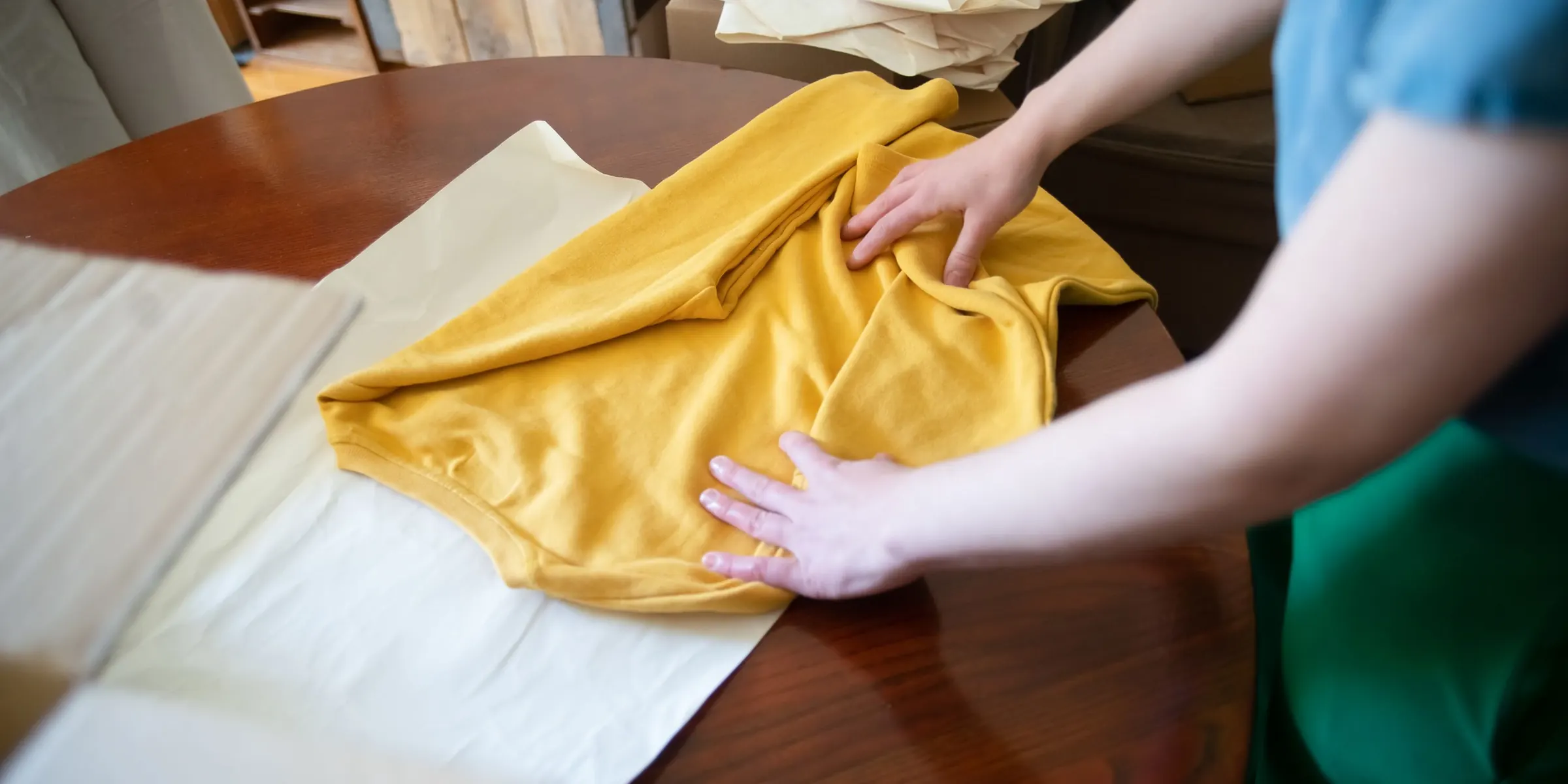 Handen die een gele trui opvouwen op een houten tafel