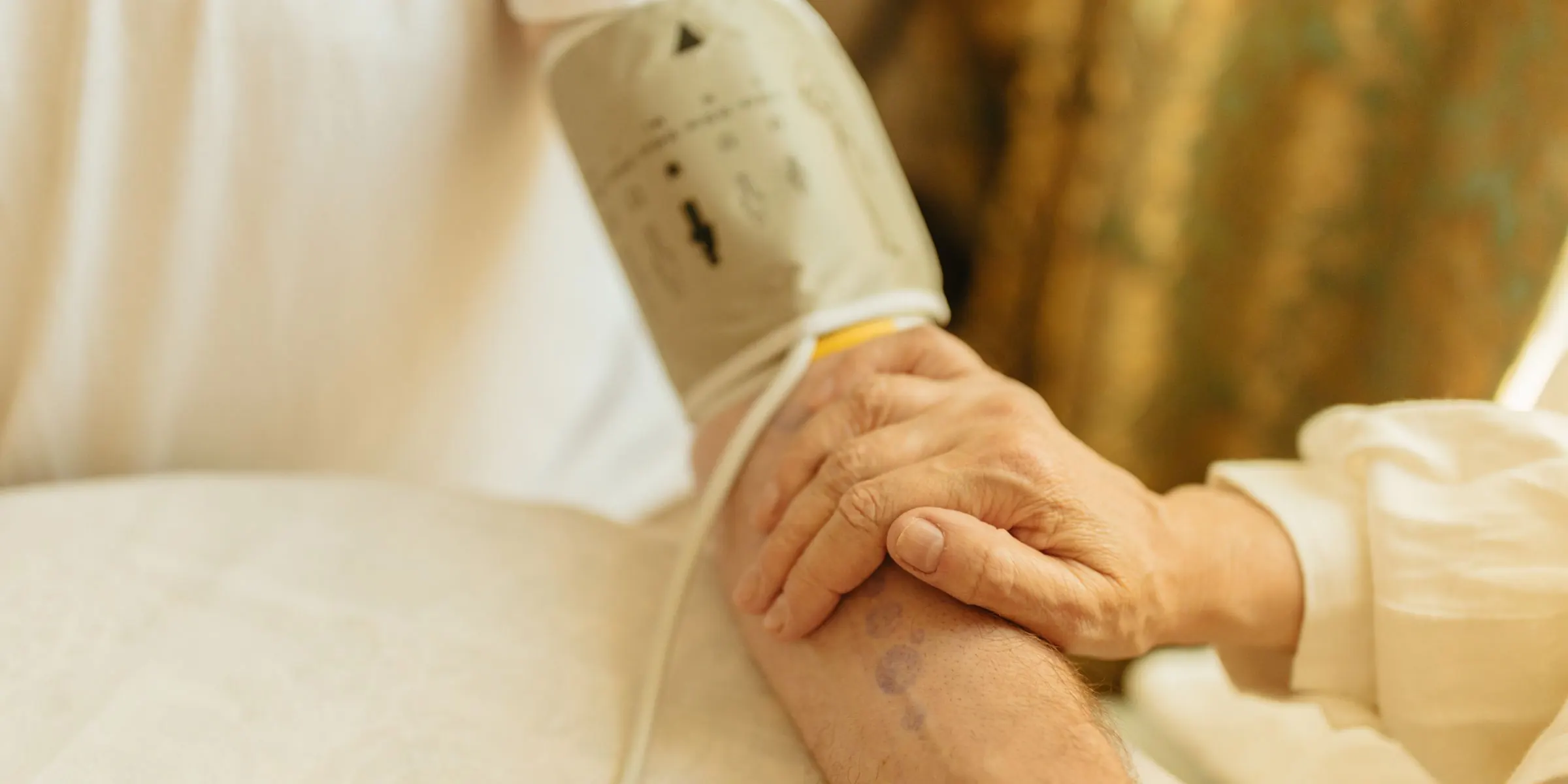 Een bloeddrukmeter om de arm van een oudere cliënt, haar hand rust op de arm