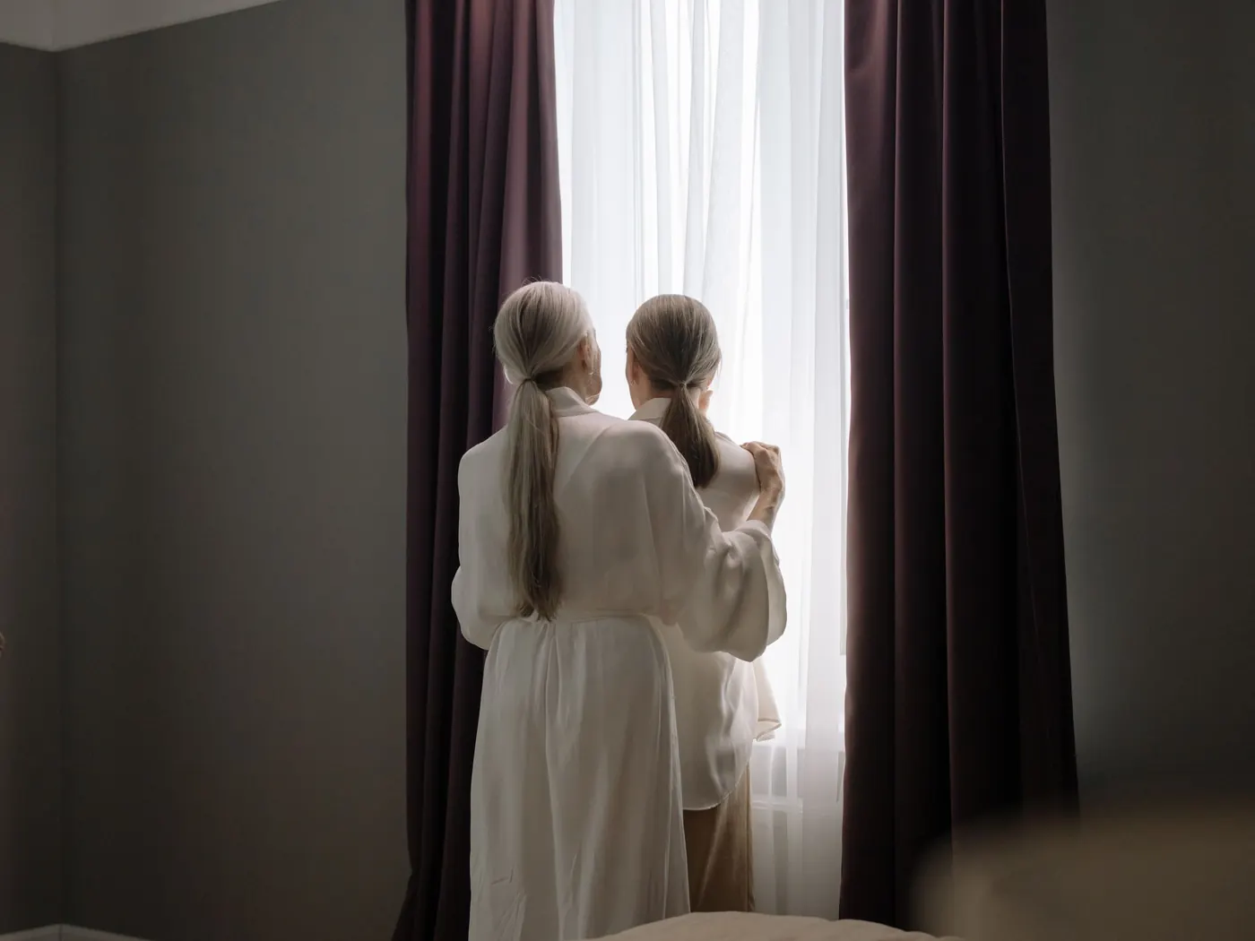 Twee oudere vrouwen staan met de armen om elkaar heen bij het raam